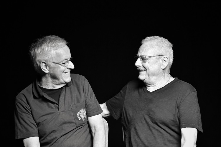 Schwarz-Weiss-Foto der beiden Brüder Peter und Kurt Bönzli. Sie sitzen einander zugewandt und lachen gemeinsam.